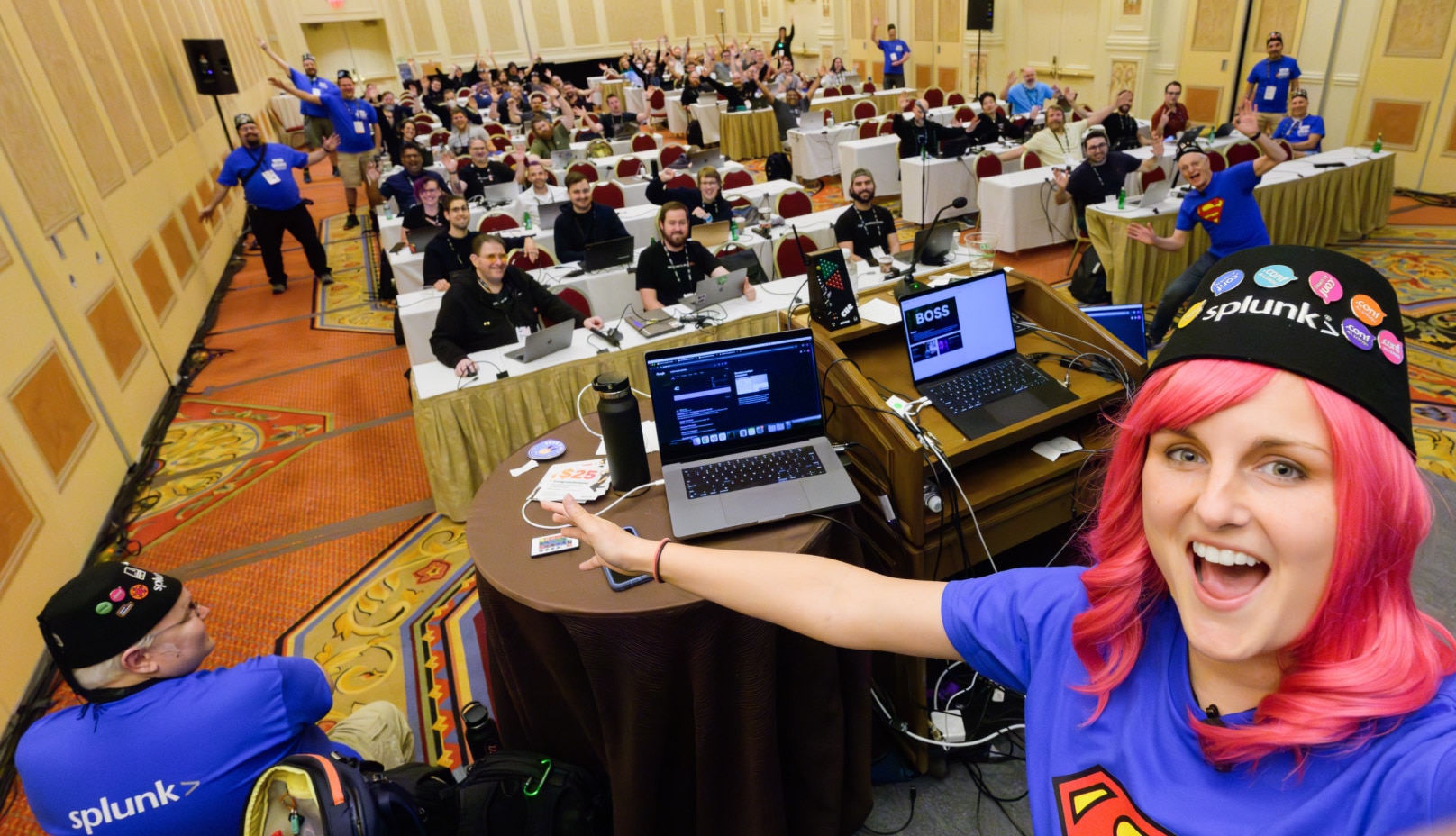 woman with pink hair and fez taking a selfie with a large working group
